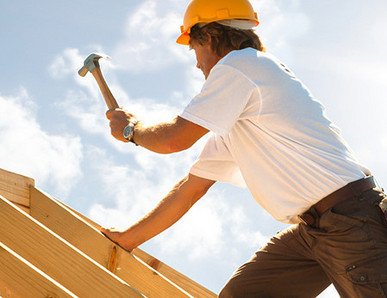 Dachdecker mit gelbem Schutzhelm beim Befestigen von Konstruktionsvollholz (KVH) auf einem Dachstuhl unter strahlendem Himmel.